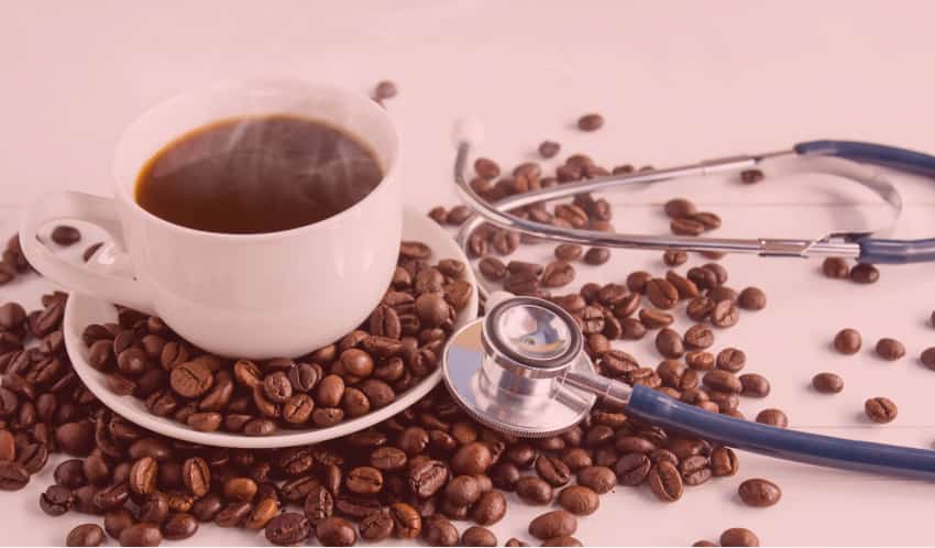 Tasse schwarzer Kaffee auf einer Untertasse, ringsum verstreute Kaffeebohnen und ein Stethoskop