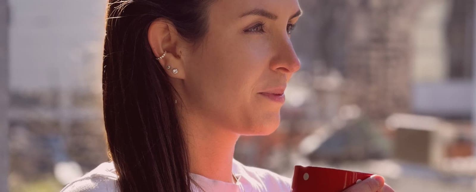Dr. Tina Mandel im Profil mit einer roten Tasse in der Hand, im Hintergrund unscharf eine Stadtkulisse