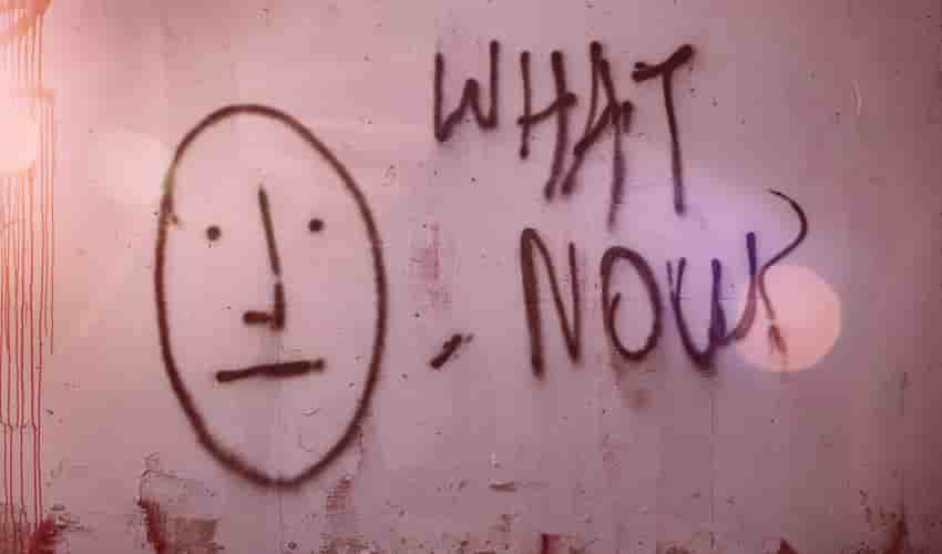 Graffiti an einer Wand: ein gemaltes ratloses Gesicht neben den Worten „What now?“